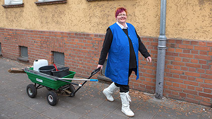 Sabine Ströhlein vor einem Haus. Sie zieht einen Handwagen mit Putzutensilien.