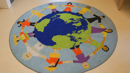 Runder Teppich mit Erdkugel und Menschen verschiedener Kulturen, die sich an den Händen halten. 