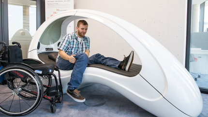 Matthias Neubauer setzt sich vom Rollstuhl in eine Ruheliege um, die wie ein Kokon geformt ist.