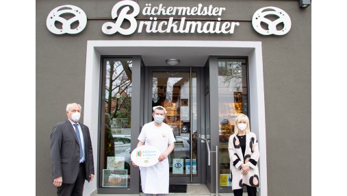 Ein Foto mit Staatsministerin Carolina Trautner sowie den Emblemträgern vor dem Eingang der Bäckerei Brücklmaier